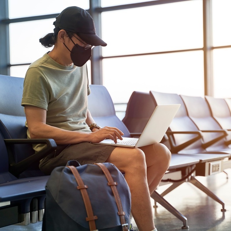 Young Asian Man Wearing A Mask While Using His Laptop At The Airport During Covid Pandemic